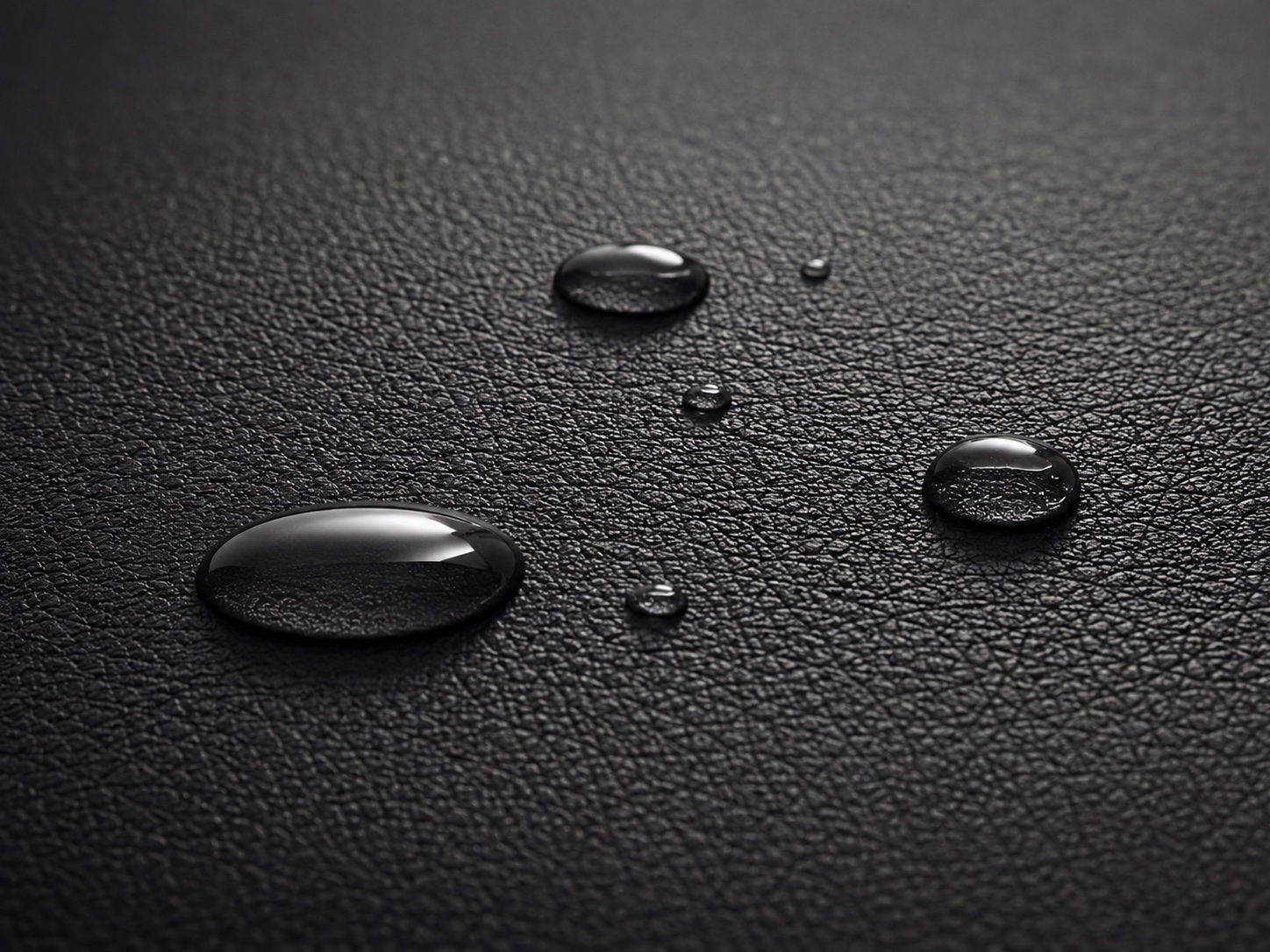 Illustrative water droplets on a black synthetic leather surface sample